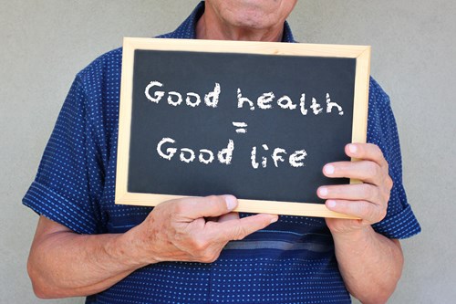 a close up of a person holding up a chalk board with Good Health = Good Live written on it. 