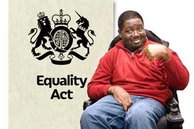 A man in an electric wheel chair pointing at an image of the Equality Act.