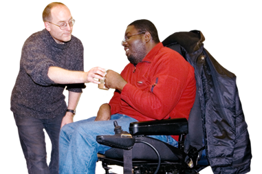 A man in an electric wheelchair being handed a drink by another man.