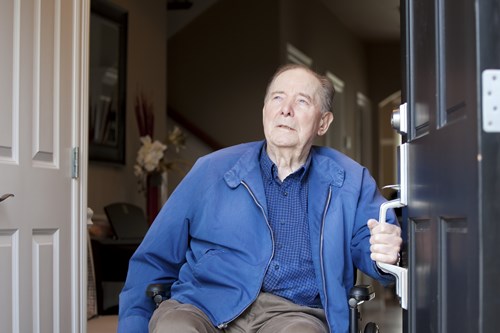 Older man in a wheelchair holding open his front door with an adapted handle.