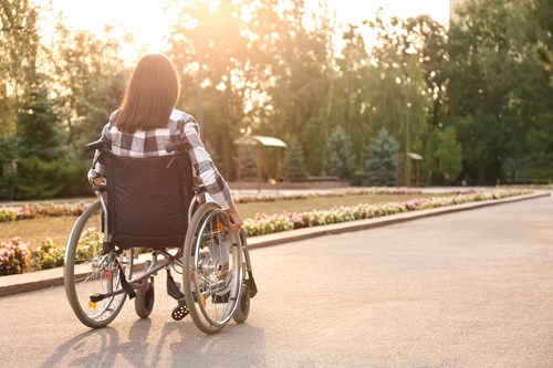 the back of a woman in a wheelchair self propelling through a park 