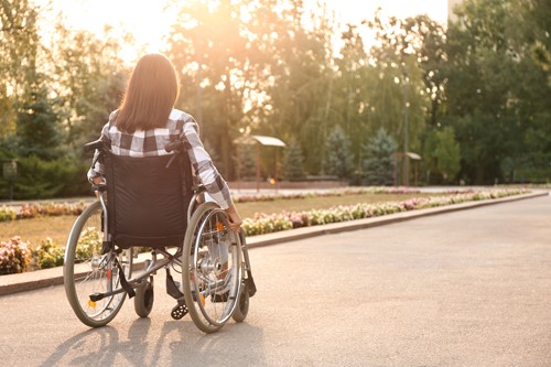 the back of a woman in a wheelchair self propelling through a park